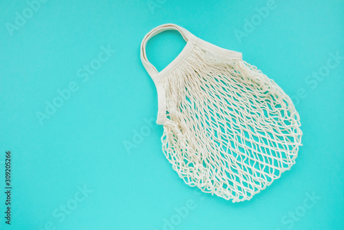 Reusable cotton net bag for shopping and food storage on mint background with copy space.