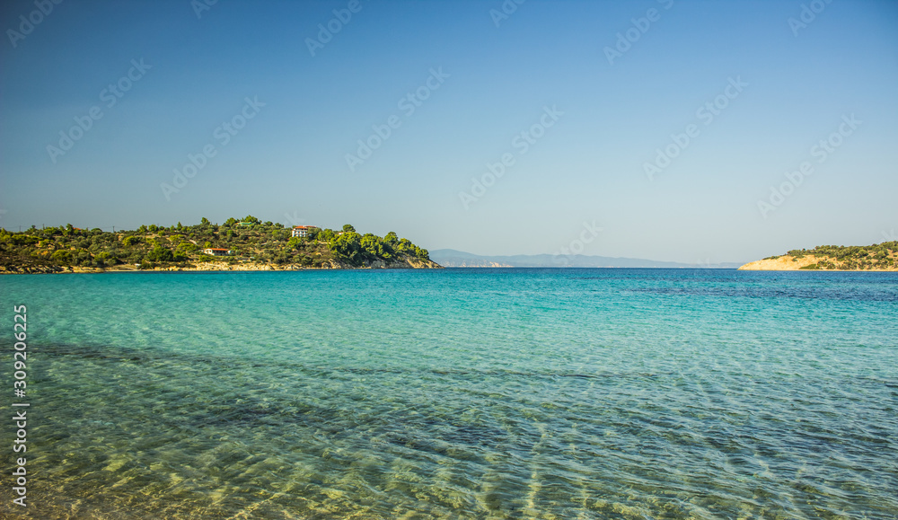 Fototapeta premium Greece beach cozy Aegean sea lagoon transparent aquamarine shallow water with horizon background view islands coast line in summer tine clear weather