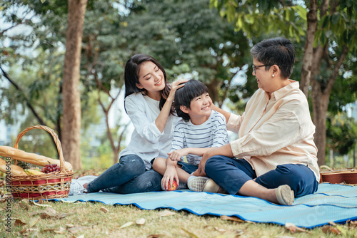 The concept of family relaxed activity in holiday.Happy Asian family mother son and grandmother enjoy picnic time at the park,spending time and have fruits in the park,lifestyle in family holiday.