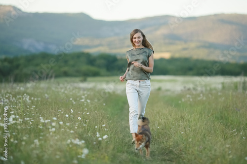 A dog and a woman running through a field of green grass.
