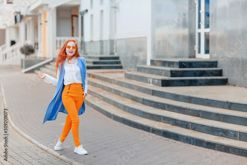Cheerful redhead young woman in bright clothes on the street.