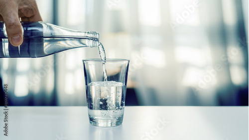 Nalewanie oczyszczonej świeżej wody do picia z butelki na stole w salonie © piotrszczepanek