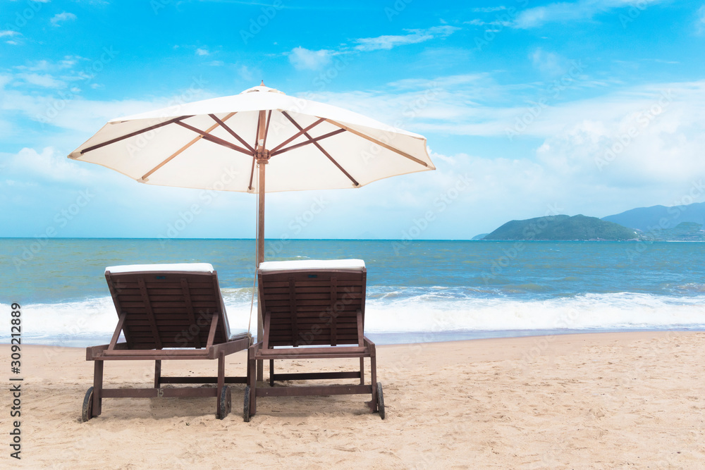 Pair of free sunbeds with sun umbrella, parasol on beautiful empty beach near clear sea sunny blue sky, golden sand. Place for relax, rest in tropical country at summertime. Vacation, freedom concept
