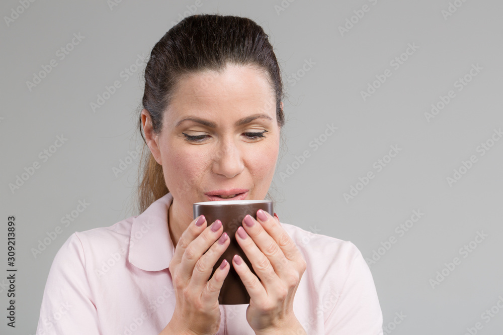 smiling middle-aged sips at a cup of fresh coffee or tea in her hand smiling middle-aged sips at a cup of fresh coffee or tea in her hand