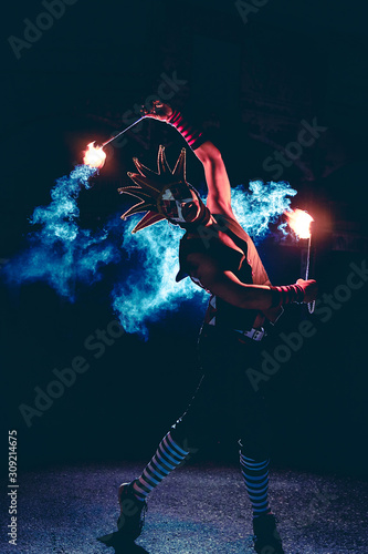 Wallpaper Mural Man in red jester costume with double fire torch performing some action moment with some blue smoke in the dark Torontodigital.ca