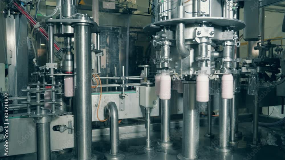 Food packaging process at a food factory conveyor. A machine fills bottles with milk at a factory. Food packaging process at a food factory conveyor. A machine fills bottles with milk at a factory.