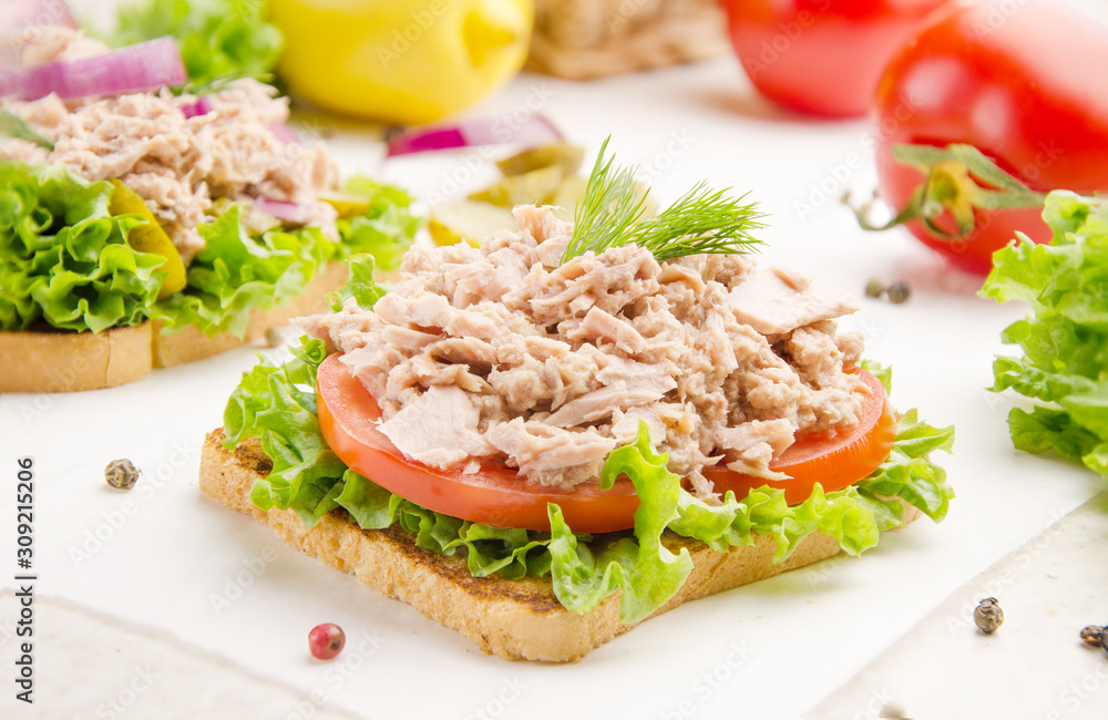 Tuna sandwiches with lettuce tomatoes and onions on parchment paper