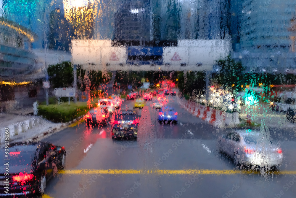 Road view through car windshield with rain drops in the evening city
