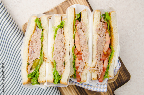 Obraz na płótnie Flat lay view at wrapped Tuna sandwiches with lettuce tomatoes pickles and onions in wicker basket cut in half w salonie
