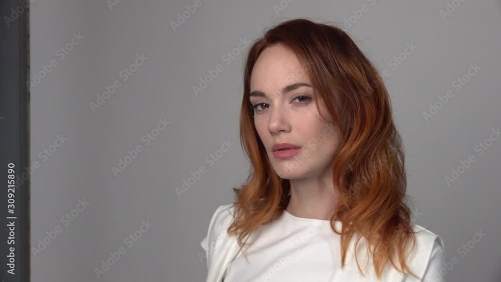 Close-up of beautiful girl with red hair. She looks into the frame, straightens her hair, seductively tilts her head radiating goodwill. Close-up of beautiful girl with red hair. She looks into the frame, straightens her hair, seductively tilts her head radiating goodwill.