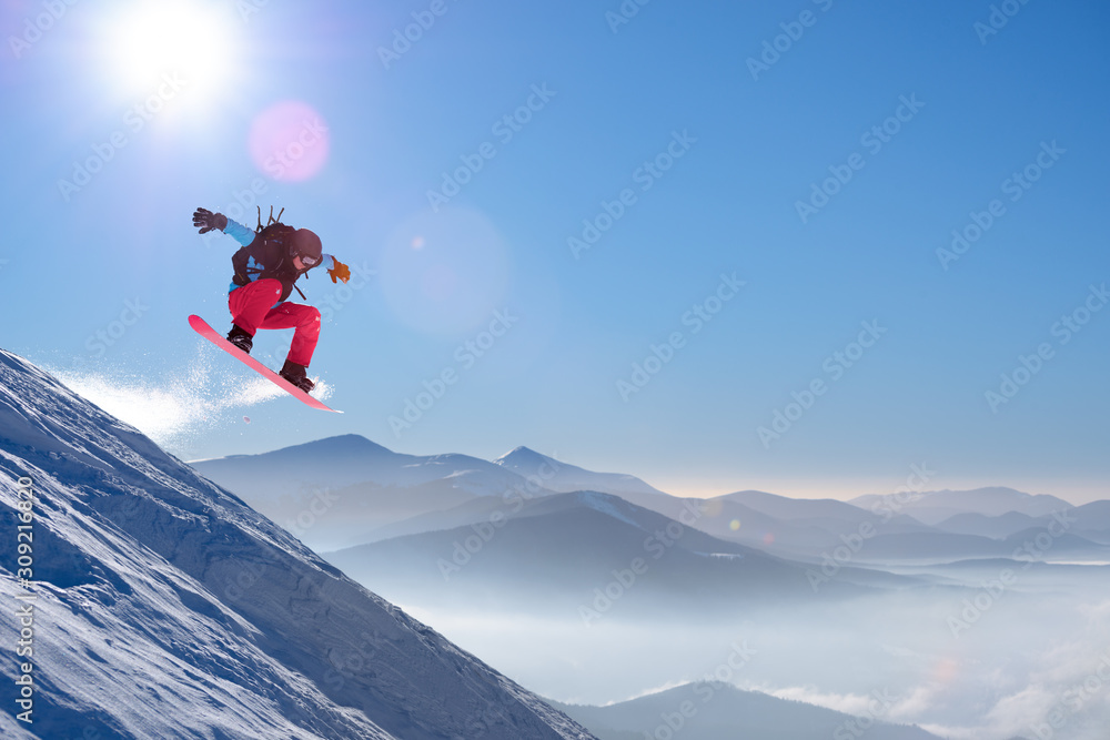 Snowboarder Jumping on Red Snowboard in Mountains at Sunny Day. Snowboarding and Winter Sports Snowboarder Jumping on Red Snowboard in Mountains at Sunny Day. Snowboarding and Winter Sports