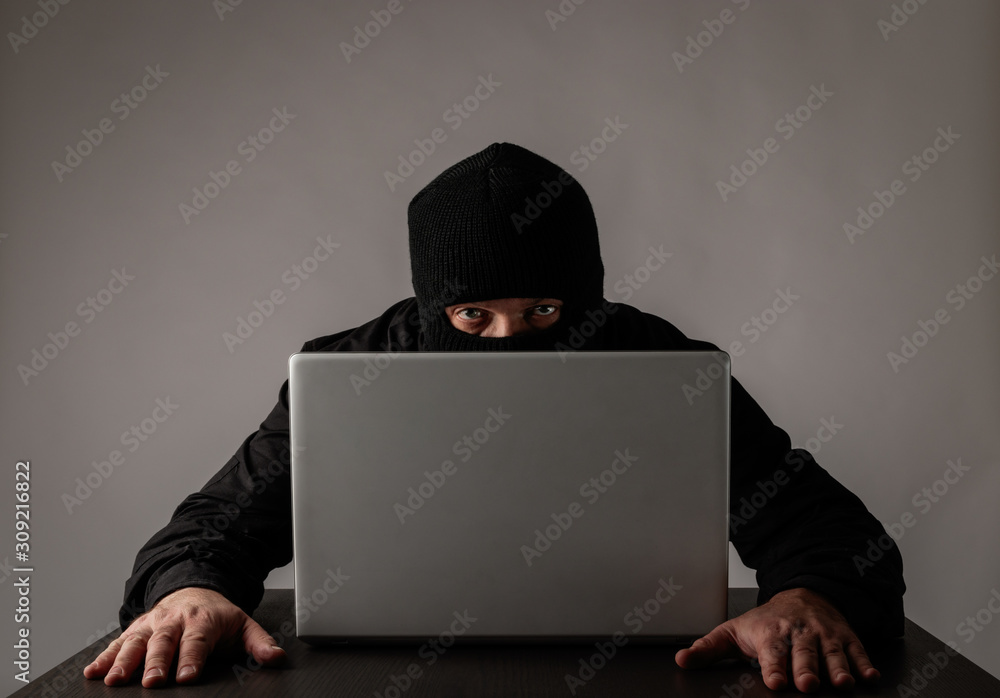Hacker in mask using a laptop. Hacker in mask using a laptop.