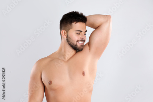 Young man showing hairless armpit after epilation procedure on light grey background