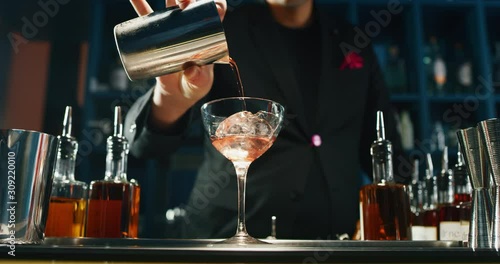 A professional bartender is preparing an alcoholic cocktail with ice cubes to customers at the bar or disco club. photo