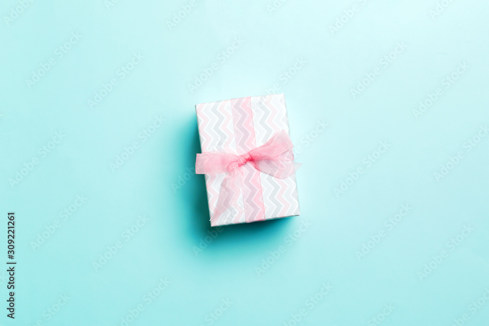 wrapped Christmas or other holiday handmade present in paper with pink ribbon on blue background. Present box, decoration of gift on colored table, top view with copy space