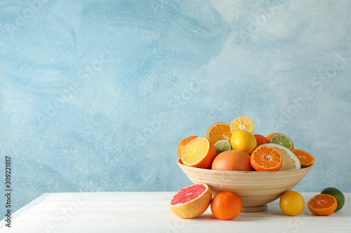 Billede på lærred Juicy citrus fruits in bowl on wooden table against blue background, space for t