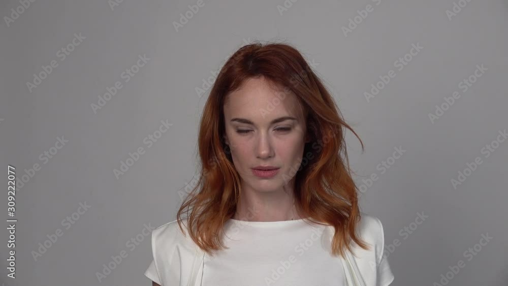 Portrait of young woman. A beautiful girl with red hair in a light blouse poses on a neutral background, wind blows hair, shoulder portrait, emotional natural look Portrait of young woman. A beautiful girl with red hair in a light blouse poses on a neutral background, wind blows hair, shoulder portrait, emotional natural look