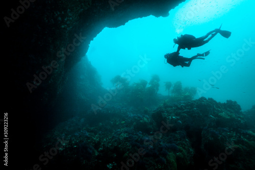 A couple of scuba divers exploring an underwater arch.