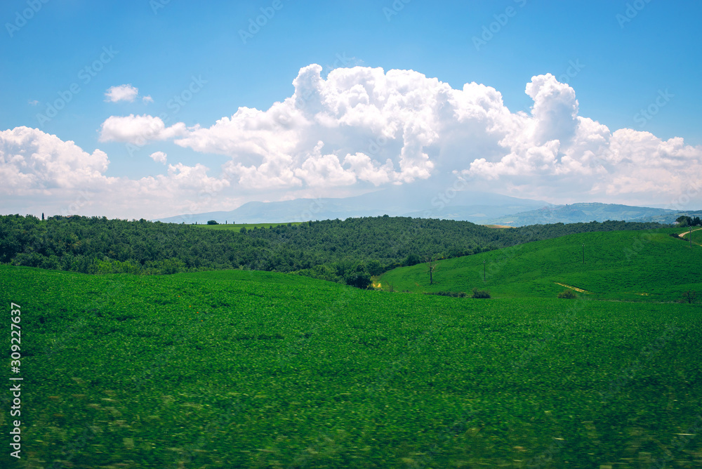 Obraz premium Fantastic summer field in Italy, Tuscany landscape with cloudy sky and fragment of stone wall.View of fields and hills of Tuscany from above the walls