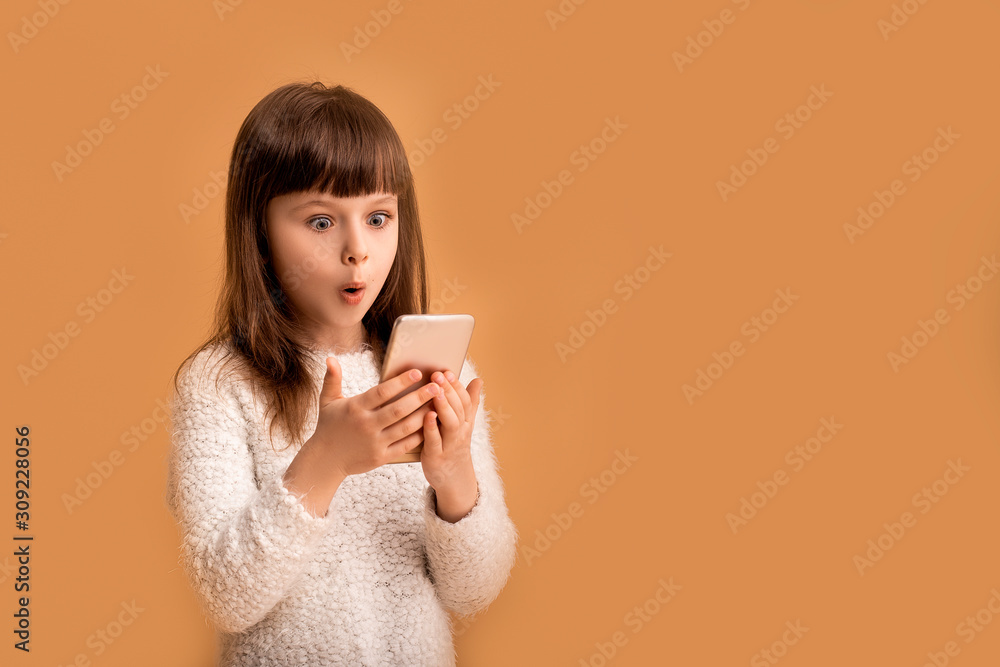 Gamer kid girl play online game on mobile phone with her school friends, technology concept. Surprised face emotion and looking to screen, looking funny child, orange background Gamer kid girl play online game on mobile phone with her school friends, technology concept. Surprised face emotion and looking to screen, looking funny child, orange background
