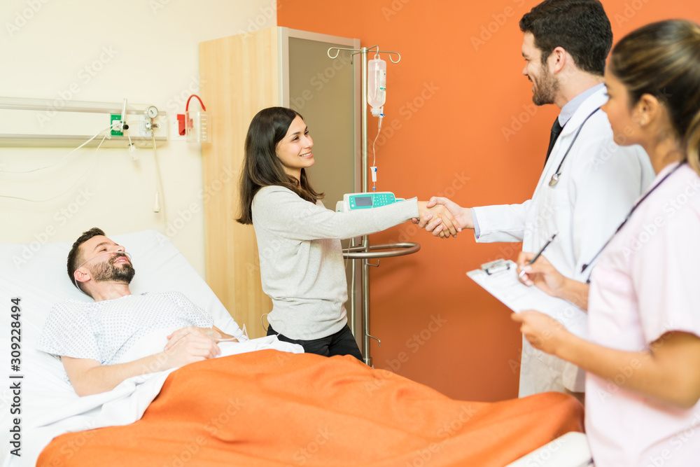 Woman Shaking Hands With Doctor While Standing By Patient Woman Shaking Hands With Doctor While Standing By Patient