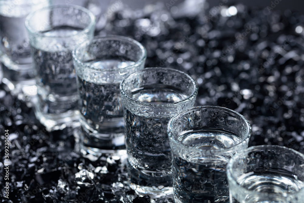 Damp glasses of vodka with ice on a black reflective background. Damp glasses of vodka with ice on a black reflective background.