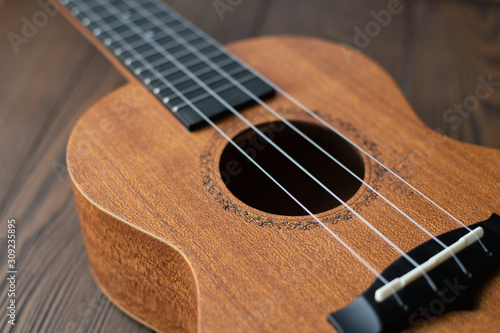 Defocused ukulele body, soundhole, bridge and neck on brown wooden background.