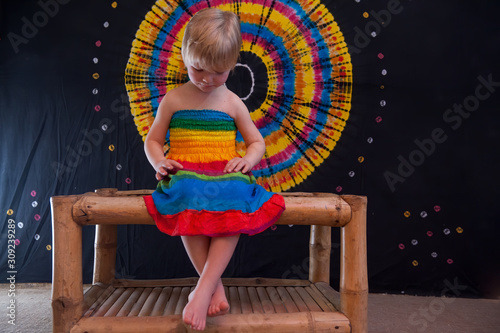 Happy Cute caucasian boy changed clothes at carnival in dress of girl of rainbow color. Blond hair. LGBT color background. Education in kindergarten and preschool children. hair coloring