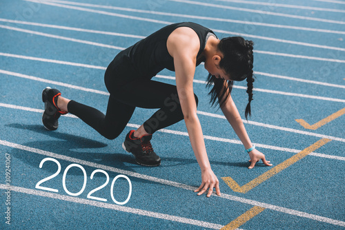 young sportswoman standing in start positing on running track near 2020 lettering