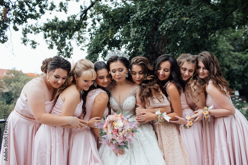 Bride with bridesmaids. Girl bride with her friends in elegant dresses. Bride with bridesmaids on the park on the wedding day. Happy girls at their best friend's wedding. 