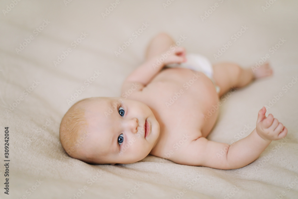 Funny little baby wearing a diaper lying on a white knitted blanket. Child nappy change and skin care. Funny little baby wearing a diaper lying on a white knitted blanket. Child nappy change and skin care.