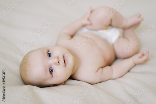 Funny little baby wearing a diaper lying on a white knitted blanket. Child nappy change and skin care. 