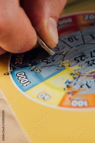 partial view of gambler scratching lottery ticket with silver coin