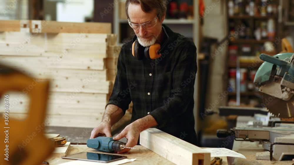 Senior carpenter wearing of protecting eyeglasses and taking drilling machine in workshop Senior carpenter wearing of protecting eyeglasses and taking drilling machine in workshop