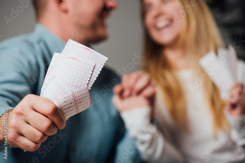 cropped view of happy man and woman holding hands while holding lottery tickets photo