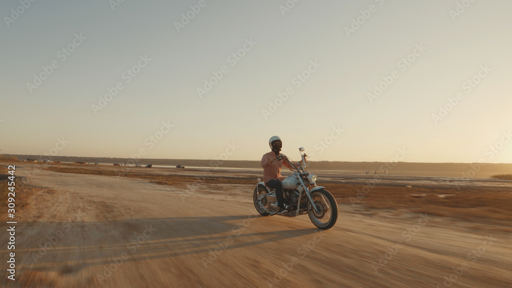 Motorcyclist driving his motorcycle on the dirt road during sunset Motorcyclist driving his motorcycle on the dirt road during sunset