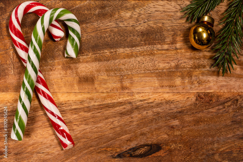 Christmas candy caramel cane on a wooden tray with a spruce branch and a Christmas toy