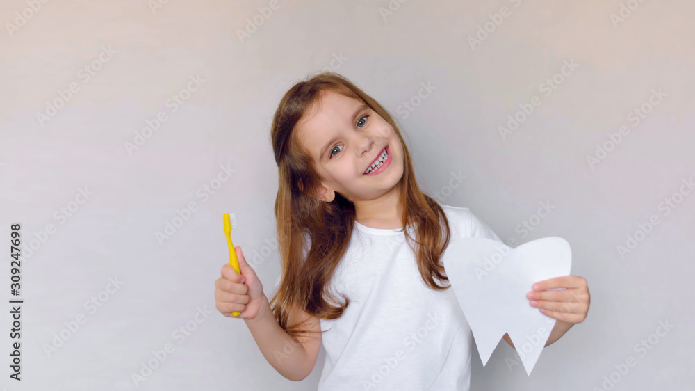 Little cute baby girl with toothbrush and tooth layout in hand. Concept of health, oral hygiene, people and beauty. The layout of the space. Selective focus. Little cute baby girl with toothbrush and tooth layout in hand. Concept of health, oral hygiene, people and beauty. The layout of the space. Selective focus.