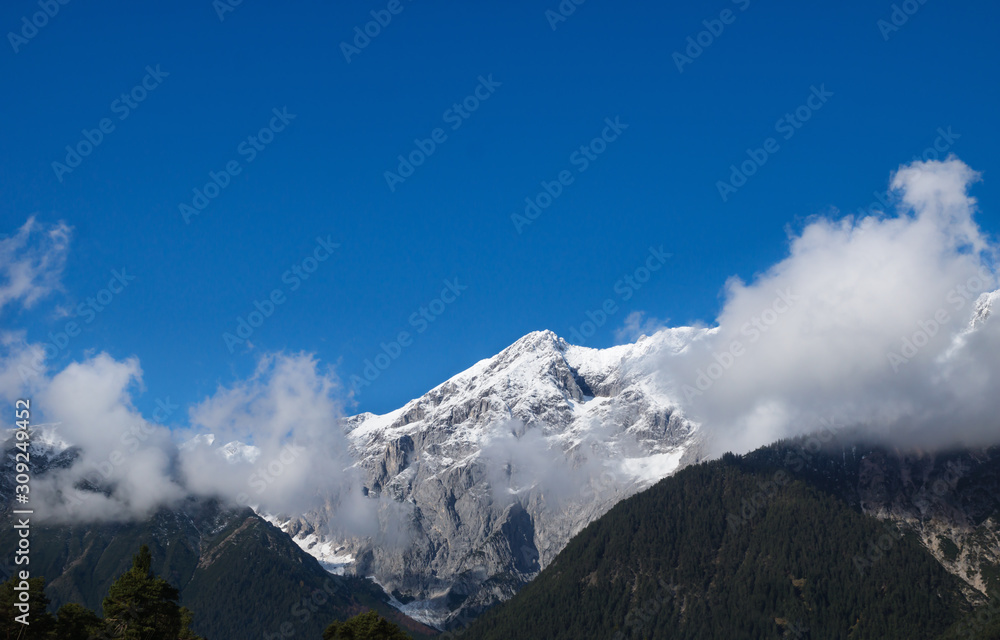 Mountain tops with snow, clouds, forest and blue cloudless sky, Wildermieming, Tirol, Austria Mountain tops with snow, clouds, forest and blue cloudless sky, Wildermieming, Tirol, Austria