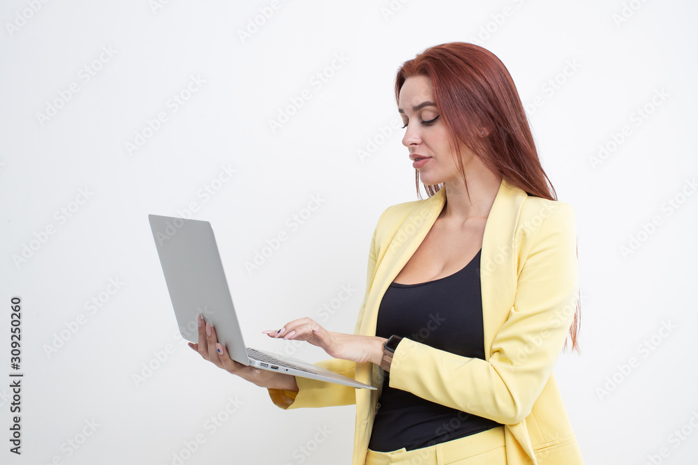 Red-haired girl in a yellow suit holding a laptop on a white background Red-haired girl in a yellow suit holding a laptop on a white background