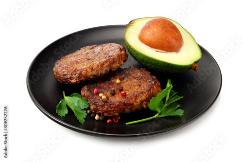 grilled burger meat with avocado on black plate isolated on white background.