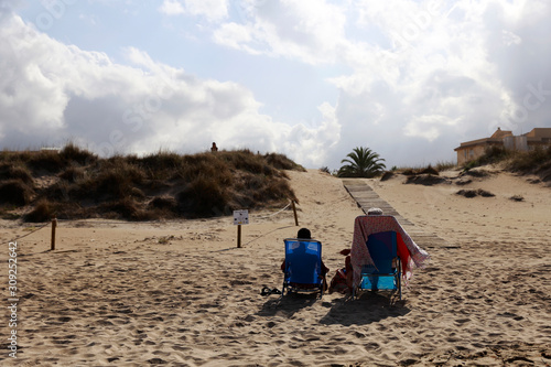 Two old people sitting on the sand beach enjoying the sun. Two tourists are sunbathing. Beautiful sand beach in Spain during the summer. 