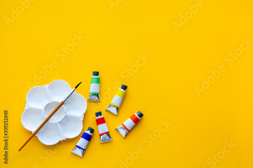 top view of brushes, color tubes and palette on yellow background, copy space, flat lay, paintings art concept