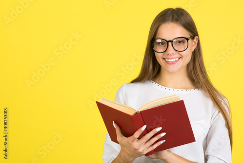 beautiful young woman in a white shirt on a yellow background in glasses with a book in her hands