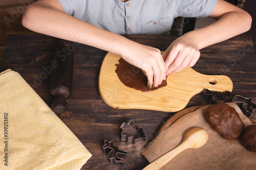 Boy's hands making traditional Christmas cookies. Raw dough and cutters for the holiday cookies on a dark wooden table. Preparing Christmas gingerbread. Steps of making biscuits. Top view.