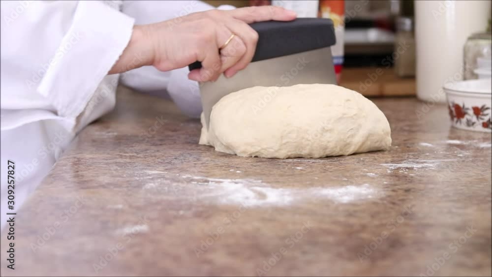 Chef cutting fresh bread dough into portions using a bench scraper. Chef cutting fresh bread dough into portions using a bench scraper.