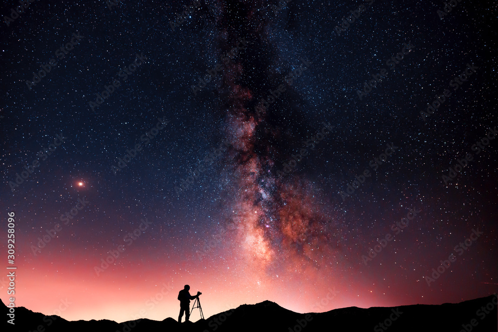 Beautiful starry night landscape. A silhouette of a photographer stands on a hill and looks at a beautiful starry sky with a bright milky way - obrazy, fototapety, plakaty 