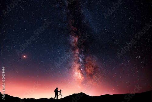Beautiful starry night landscape. A silhouette of a photographer stands on a hill and looks at a beautiful starry sky with a bright milky way
