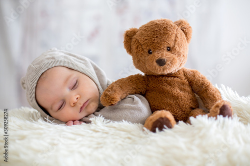 Sweet baby boy in bear overall, sleeping in bed with teddy bear photo