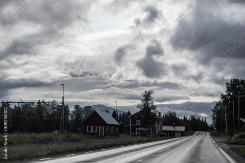 Dramatic northern scandinavian route with red traditional swedish houses. Cold northern europe freeway. Nature forest, mountains road perspective view. Travel scenery. © Kathrine Andi